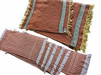 Two rust-colored vintage hand woven mats with fringed ends, one smaller with yellow fringe and patterned band, one longer with white fringe and striped pattern