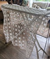 Full tablecloth draped on a drying rack showing length, square pattern of crochet lace with fabric inserts, beige color.