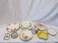 Nine assorted Limoges porcelain pieces including plates, bowls, ashtrays, and covered sugar bowl arranged on white fabric background.