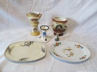 Six porcelain items on display: two vases with floral and bird motifs, two platters with hummingbird and floral patterns, small miniature vase, and candle holder.