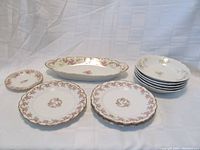 Five salad plates, three soup bowls stacked, and one celery dish all decorated with pink floral patterns and gold trim. Pieces arranged to show quantity and style.