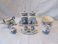 Full set of Delft Blue porcelain items showing bowl, tea caddy with tray, condiment set with tray, cow creamer, miniature jug, and miniature pitcher.