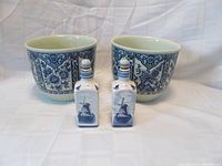 Full set photo showing two large flower pot jardinières and two porcelain cruets in front on a white surface with white backdrop