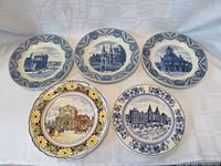 Set of five Delft collector wall plates with Dutch landmark designs, showing blue and white ceramic with one multicolored floral border plate.