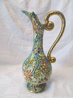 Front and side view of the colorful majolica pitcher vase showing intricate floral relief and large gold-colored handle.