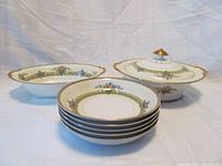 Five coupe-style soup bowls stacked together with the covered serving dish and oval serving dish in the background, showing floral and gold band pattern on white porcelain.