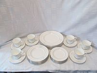 Full set layout showing six dinner plates, six salad plates, six bread & butter plates, and six teacup and saucer pairs all white with delicate floral embossing and silver trim.