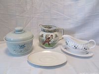 Four Royal Doulton porcelain items: covered round casserole with lid, colorful bird and floral pattern pitcher, white gravy boat with blue floral pattern and underplate, light blue-gray bird design gravy dish