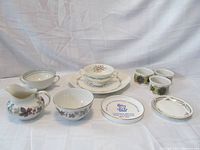 All porcelain items arranged including serving platter, bowls, plates, creamer and sugar bowl set, ramekins, and souvenir ashtray.