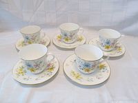 Five teacup and saucer sets arranged on white background showing floral design and gold accents.