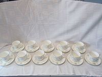 Eleven Royal Doulton teacup and saucer sets arranged in rows on a white cloth background.