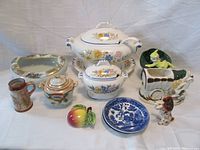 Overview of ten-piece porcelain and ceramic lot including transferware tureens, planters, figurines, saucers, flower bowl, lusterware sugar bowl, stein vase, and wall decoration.