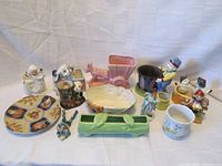 Full view of all 14 porcelain items arranged on a white surface, displaying planters, figurines, bowl, and plate.