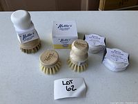 Photo showing three wooden brushes with natural bristles and a box of Nellie's dish soap powder, all new and eco-friendly.