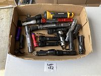 Box containing multiple flashlights of different sizes and colors including black, silver, red, purple, and yellow. Flashlights have different designs and some have wrist straps.