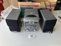 Full view of the KOSS mini stereo system including the central unit with CD player and two external speakers on a table with original box in background.