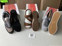 Full shot of three pairs of shoes in front of SOUL shoeboxes, showing brown leather sandals with buckles, beige-gray leather sneakers, and gray textile sneakers