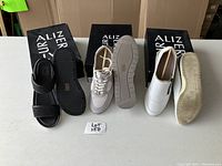 Overview photo showing three pairs of Alizar shoes: black leather sandals, beige runners, and white slip-ons, with all soles visible.