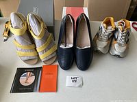 Overview of all three pairs of shoes: yellow leather sandals, black leather loafers, and white and orange runners with accompanying box and booklets