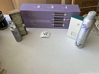 Photo shows the lot contents on a white table including the boxed blowout brush set, thermal protectant spray bottle, hair bandeau, and a hairspray canister.