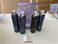 Four MONAT bottles standing upright next to a purple carrying pouch, with labels visible.