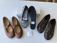 Three pairs of women's shoes displayed on white surface with a lot number card. Includes brown Mary Jane shoes, black and white print slip-ons, and brown woven design slip-ons.