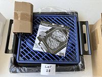 Top photo of the blue electric mini grill with handles, user manual placed on top showing product and branding information.