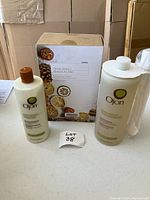 Three bottles of Ojon shower products on table with cardboard box behind. Products include shampoo, conditioner with pump, and body wash.