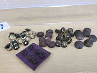 Buttons including black and champagne acrylic rectangular buttons, round matte pink and brown with Greek key pattern, round black with gold marbling, and textured black with square pattern.