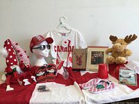 Photo showing assorted red and white Canada Day items on a table including T-shirt, cap, sunglasses, flip flops, plush gnomes, Canadian flags, moose plush, and other items.