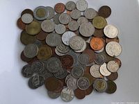 Pile of assorted foreign coins on white background showing various sizes, colors and designs from multiple countries.
