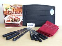 Overview of kitchen knife set, cutting board, apron, and cookbook arranged on table.