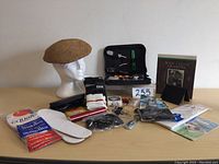Full view of men’s lot arranged on wooden surface including hat, tool kit, insoles, gloves, wrist bands, hand warmer, insulated mug, wallet, wristwatch, and book