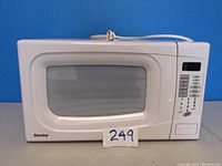 Front view of the white Danby microwave showing the door with window and keypad controls on the right. Power cord coiled on top.