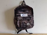 Full front view of the knapsack showing the camouflage print, front pocket, shoulder straps and carry handle.