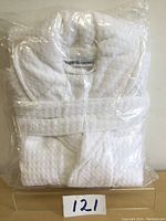 White cotton bath robe folded and packaged in clear plastic, showing texture and brand label 'WHITE SEASONS'