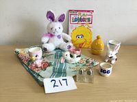 Photo showing the entire lot on a floral cloth with a stuffed bunny, four egg cups, yellow salt and pepper shaker, and the children's book