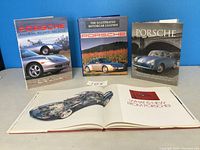 Four hardcover Porsche books standing and one open showing an illustration of a Porsche car's internal construction.