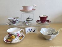 Photo of all tea cups with matching saucers, jam dish, sugar bowl, and spreaders arranged on display stands.