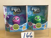 Front view showing two new in box Fijit Friends Newbies interactive toys, pink and green.