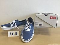 Pair of new Mens VANS Skate Authentic shoes in blue shown on clear stand with original box in background. Size 7 label visible on box.