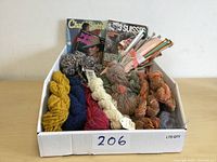 Box containing multiple skeins of yarn in various colors, knitting needles in bag, and two vintage knitting pattern books.