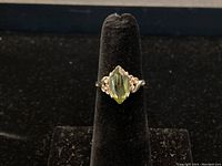 Front view of ring on black stand showing marquise-cut green peridot and scroll shoulders