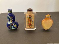 Three vintage snuff bottles showing general shapes and colors: blue cloisonne floral, clear rectangular glass with painting, amber-colored bottle.