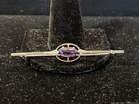 Front view of brooch on display stand showing oval amethyst in center of bar setting