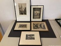 Five framed antique etchings laid out on table, showing various urban architectural and landscape scenes.