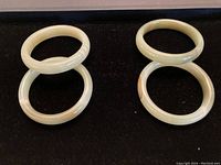 Four smooth, polished agate stone bangles arranged on black fabric, showing light green to cream colors and natural banding.