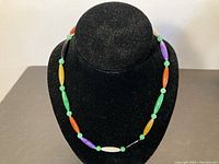 Full view of necklace displayed on black stand showing the various colored elongated jade beads and green round beads