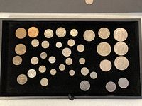 Photo showing all coins laid out in a tray with black velvet background, including small, medium and large silver-colored coins, some with distinct markings and portraits.