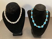 Two necklaces displayed on black velvet stands: left is pearl necklace with sterling silver clasp, right is turquoise and pearl necklace with 14kt gold clasp.